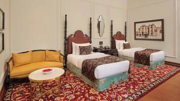 Une chambre d’hôtel avec deux lits, un canapé, une petite table ronde et un tapis à motifs.