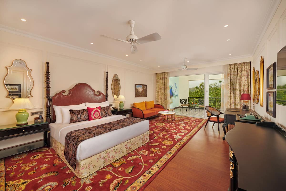 A spacious hotel room with a large bed, a sitting area with a sofa and chairs, a desk, and a balcony with a view.