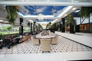 A spacious indoor area with a patterned floor, wicker furniture, and hanging plants.