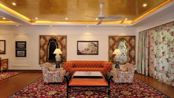 Una habitación con un sofá capitonado, sillones estampados, alfombra roja y decoraciones ornamentales en las paredes.