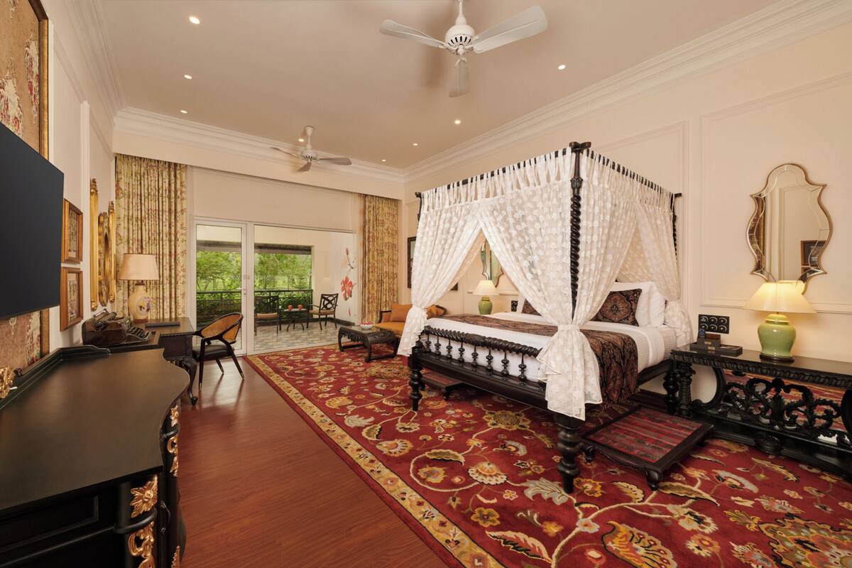 A four-poster bed with a canopy, a desk with a chair, a large mirror, and a red patterned rug.