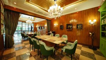 A dining area with a large table, green upholstered chairs, chandeliers, and wooden paneling.