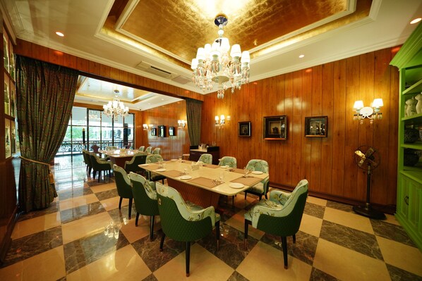 A dining area with a large table, green upholstered chairs, chandeliers, and wooden paneling. - Mayfair Tea Resort Siliguri (Siliguri)