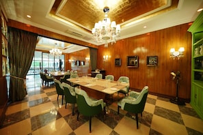 A dining area with a large table, green upholstered chairs, chandeliers, and wooden paneling. - Mayfair Tea Resort Siliguri (Siliguri)
