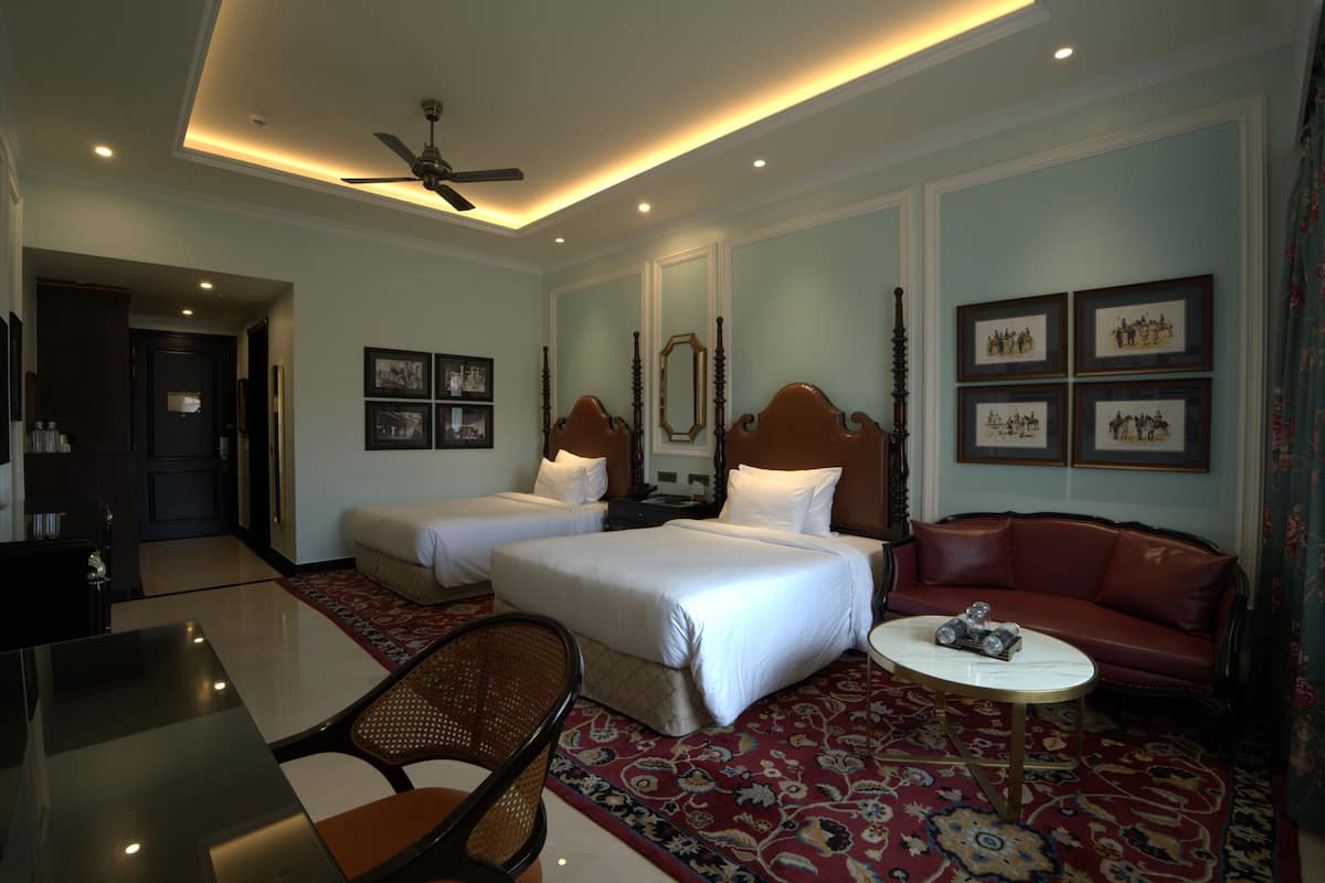 A hotel room with two beds, a sofa, a dining table, and a ceiling fan.