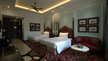 A hotel room with two beds, a sofa, a dining table, and a ceiling fan.