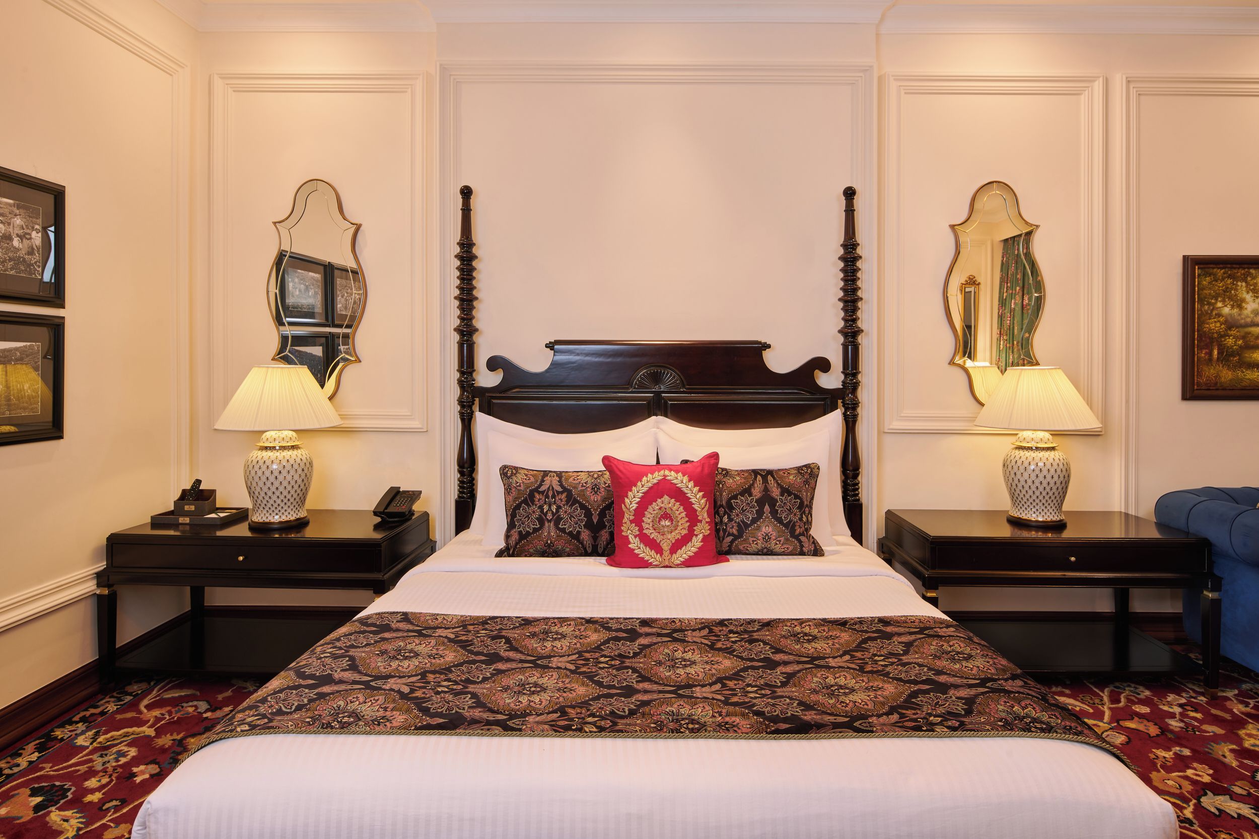 A four-poster bed with a red pillow, two bedside tables with lamps, and a blue armchair.