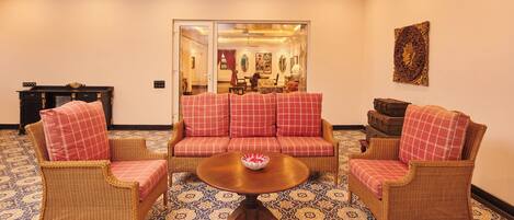 A room with a sofa set, two armchairs, a round table, and patterned floor tiles.