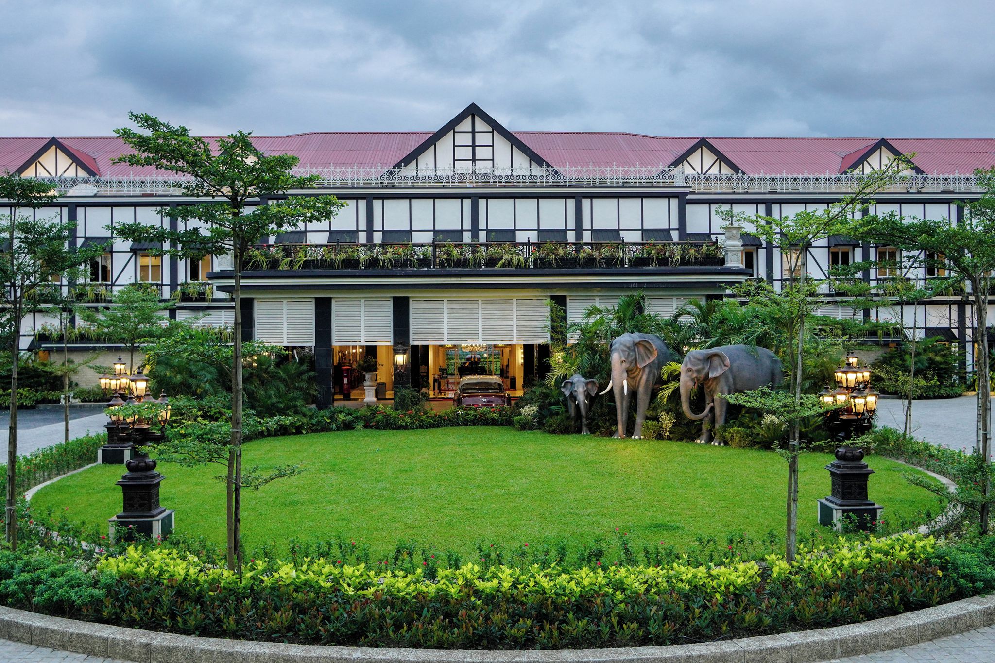 Un hôtel de style architectural traditionnel, avec un toit recouvert de tuiles rouges et un jardin bien entretenu agrémenté de deux statues d’éléphants.