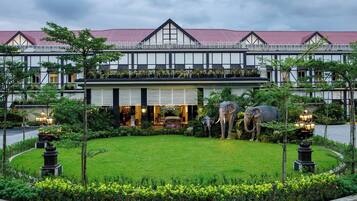 Un hôtel de style architectural traditionnel, avec un toit recouvert de tuiles rouges et un jardin bien entretenu agrémenté de deux statues d’éléphants.