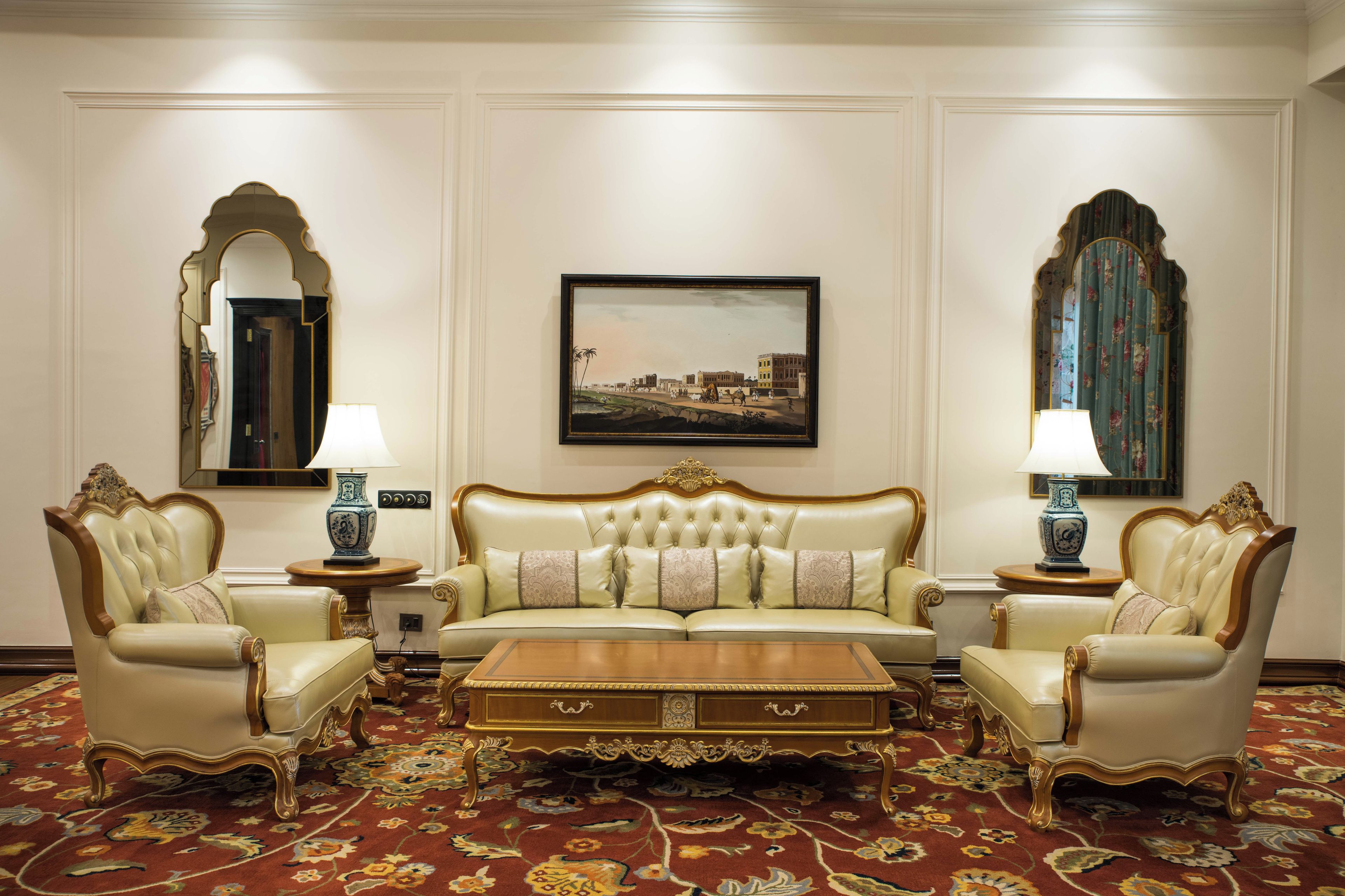 Un elegante salón con un sofá capitonado, dos sillones, una mesa de centro de madera y una alfombra estampada.