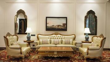 Un elegante salón con un sofá capitonado, dos sillones, una mesa de centro de madera y una alfombra estampada.