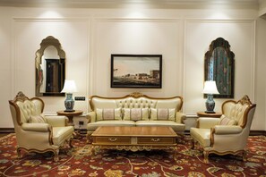 Un elegante salón con un sofá capitonado, dos sillones, una mesa de centro de madera y una alfombra estampada.