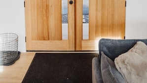 A wooden double door with a keyhole and a small window, a black doormat, and a gray sofa with a white throw pillow. - Kestrel House At The Running Y (Klamath Falls)