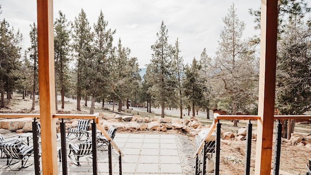 A patio area with outdoor seating, a stone pathway, and a view of a forested landscape. - Kestrel House At The Running Y (Klamath Falls)