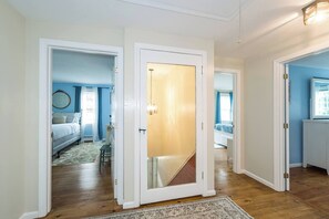 A hallway with a wooden floor, a white door with a glass panel, and a blue room with a bed and a window. - Peaceful 4- Bedroom house, Perfect for families. Close to main beaches (Yarmouth)