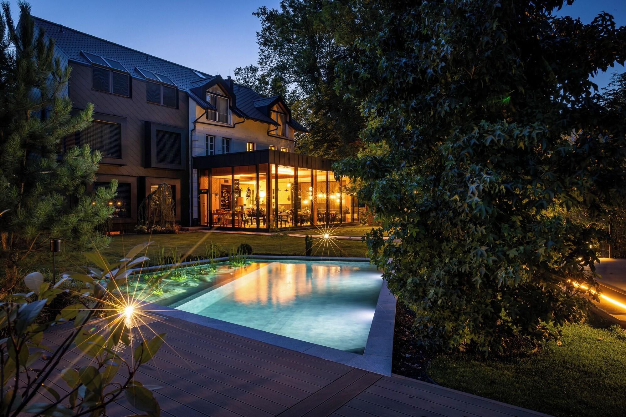 Une maison moderne avec une piscine, entourée d’arbres et d’une pelouse bien entretenue.
