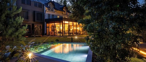 A modern house with a swimming pool, surrounded by trees and a well-maintained lawn.