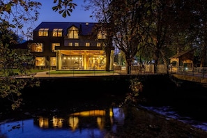 A two-story building with a glass facade, a small bridge, and a reflective water body. - Sunrose 7 Heritage Boutique Hotel (Bohinj)