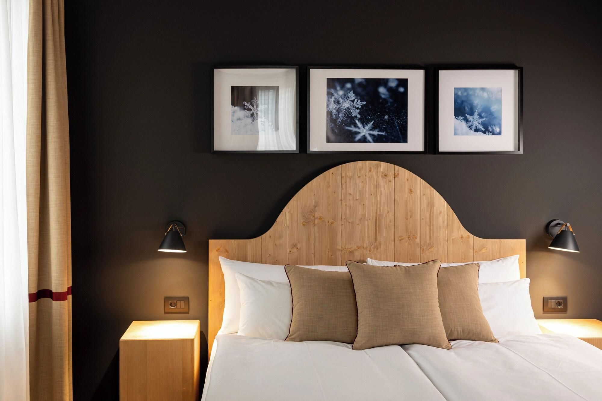 A hotel room with a wooden headboard, white bedding, and three framed pictures on the wall.