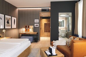 Una camera d'albergo moderna con un letto, una scrivania, un divano e un bagno parzialmente visibile da una porta aperta.