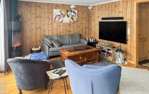 A cozy living room with a grey sofa, a blue armchair, a wooden coffee table, and a fireplace. - Gorgeous home in Sjusjøen with WiFi (Sjusjøen)