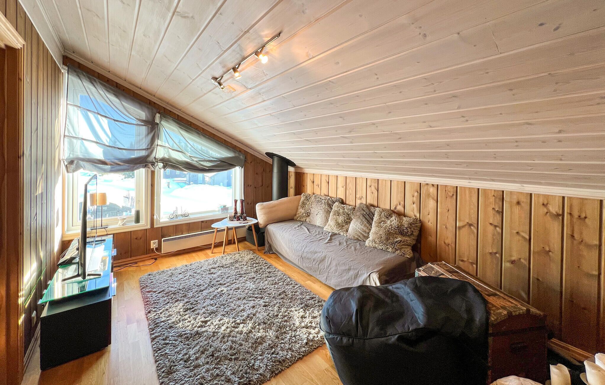 A cozy loft bedroom with a large window, a sofa, a rug, and a black ottoman.