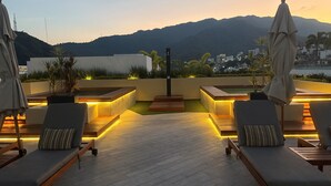 Eine Dachterrasse mit Sitzgelegenheiten und stimmungsvoller Beleuchtung, mit Blick auf Stadt und Berge.