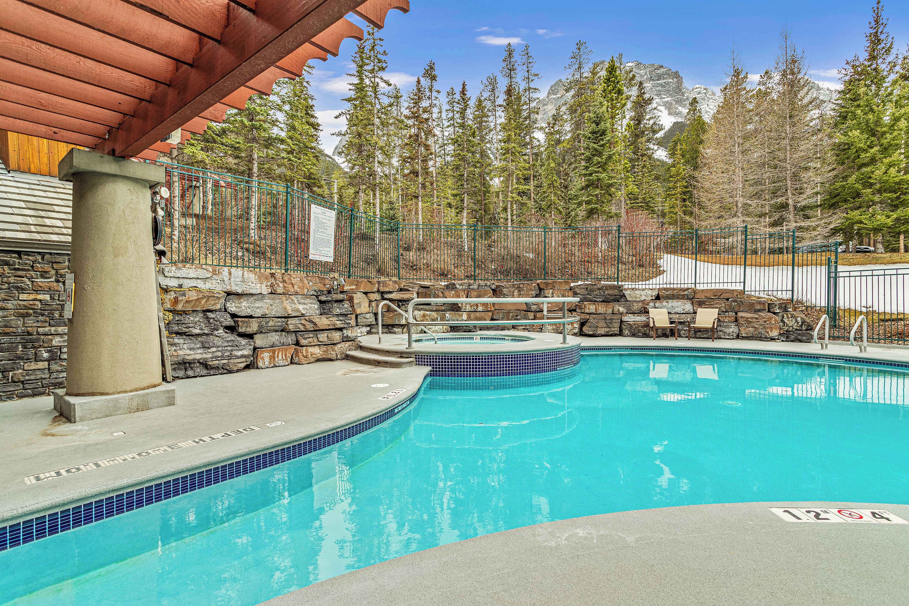 En swimmingpool med en mur av sten och en pergola av trä.