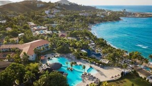 Un complexe hôtelier doté d’une grande piscine, de palmiers et offrant une vue sur l’océan.