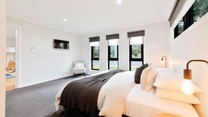 Une chambre moderne avec un grand lit, un fauteuil, une télévision et une vue sur l’extérieur.