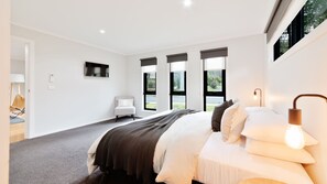 Ein modernes Schlafzimmer mit einem großen Bett, einem Sessel, einem Fernseher und Blick ins Freie.