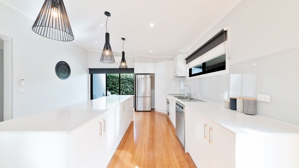 Une cuisine moderne avec des meubles blancs, des appareils en acier inoxydable et des luminaires suspendus.