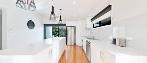 Cocina moderna con armarios blancos, electrodomésticos de acero inoxidable e iluminación colgante.
