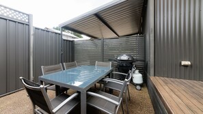 Eine Terrasse im Freien mit Tisch, Stühlen, einem Grill und einer Gasflasche.