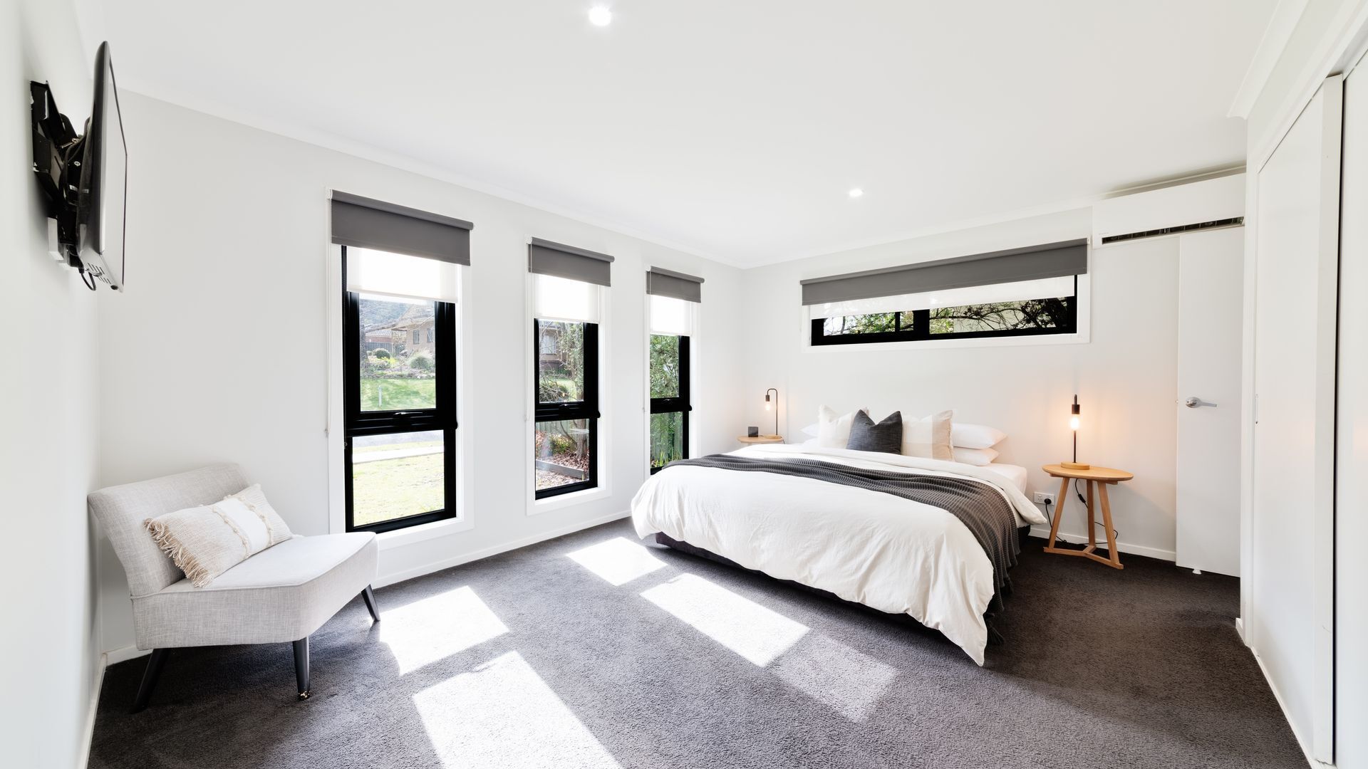 A modern bedroom with a bed, a chair, a bedside table, and large windows.