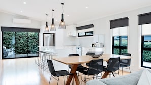 A modern kitchen with a central island, black chairs, and pendant lighting. - Snowgum Bright 1 - 3 Bedroom, 3 Bathroom (Bright)