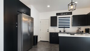 Una cocina moderna con armarios negros, un refrigerador de acero inoxidable, una cafetera y un letrero que dice 'blessed'.