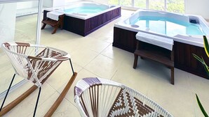 Een ruime binnenruimte met twee jacuzzi's, een groot raam en een rieten stoel.