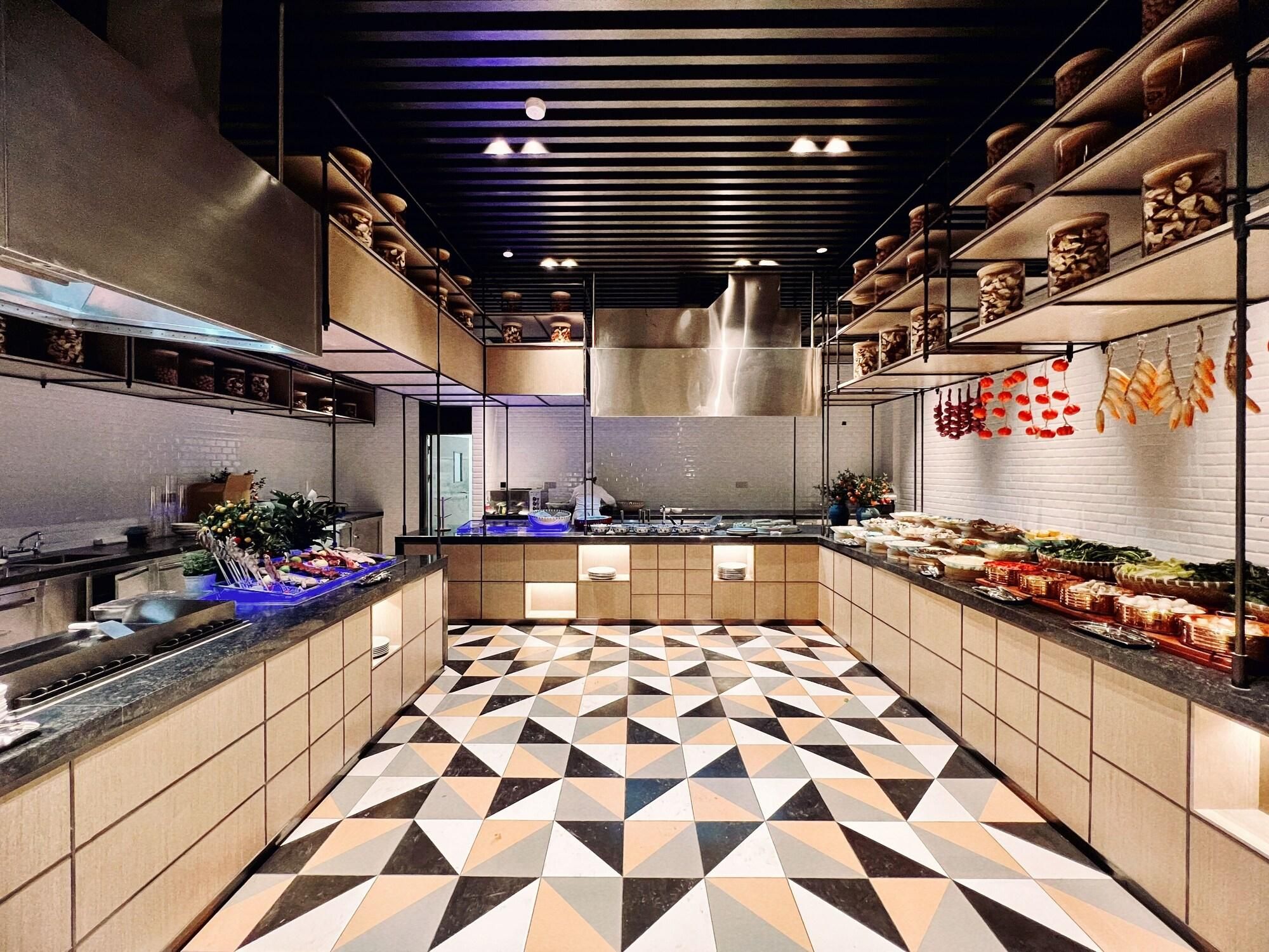 Una cocina moderna con suelo de diseño geométrico, electrodomésticos de acero inoxidable y diversos alimentos exhibidos en estanterías.