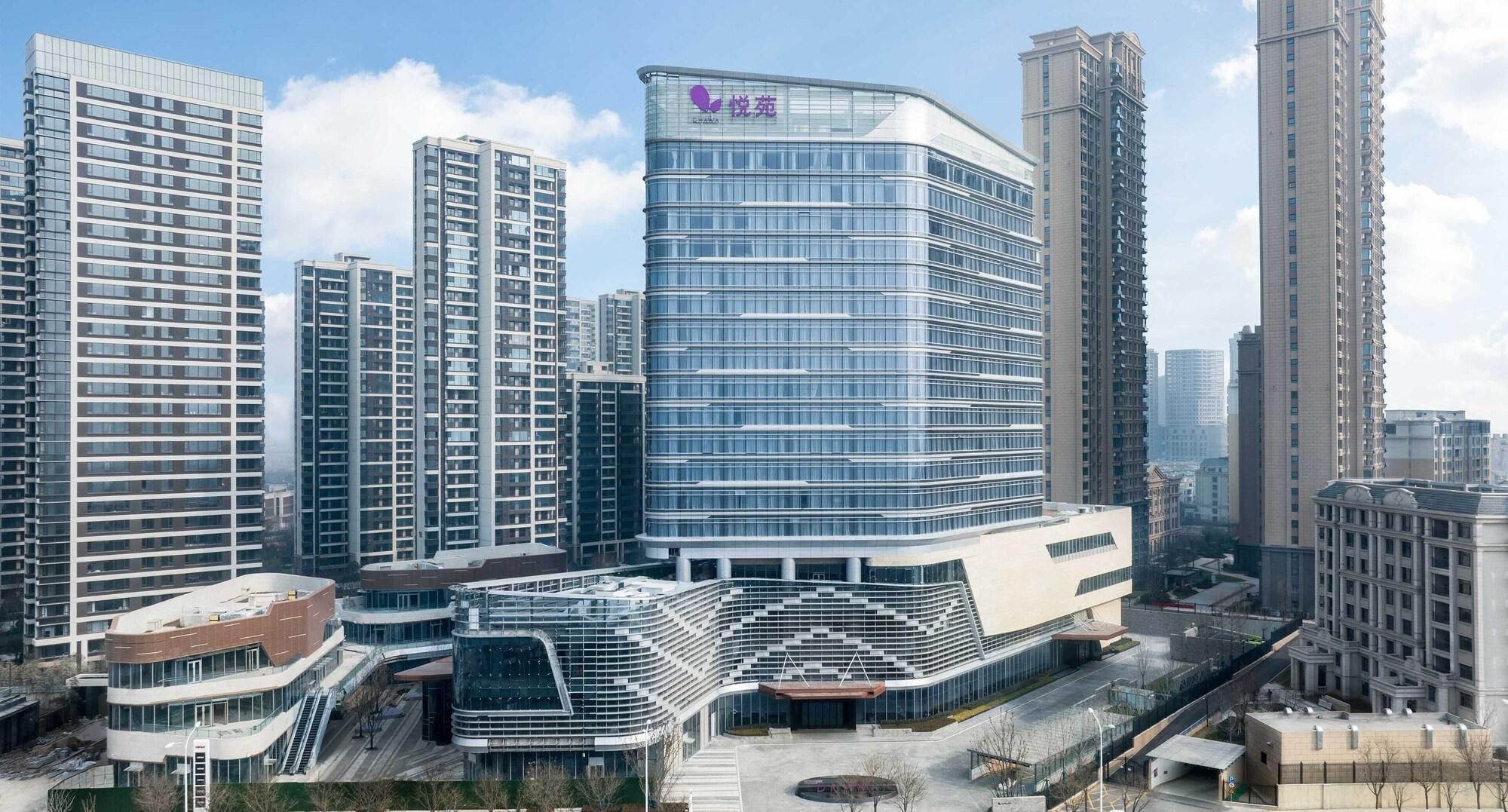 A modern hotel with a curved glass facade, surrounded by high-rise buildings.