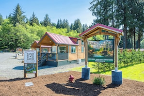 A cabin-style retreat with a red roof, a signboard advertising nightly lodging and monthly rentals, and a QR code for booking.