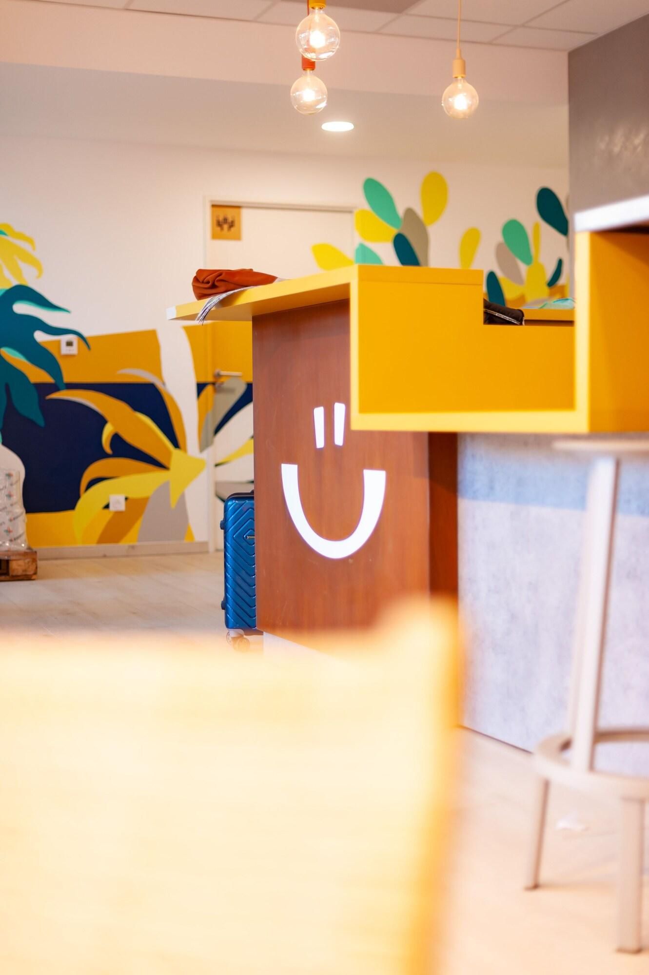 Een kamer met een houten bureau, een vrolijke gezichtsuitknip en kleurrijke abstracte muurdecoratie.
