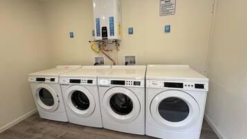 A laundry room with four Whirlpool washers and dryers, a water heater, and a notice board with laundry room rules.