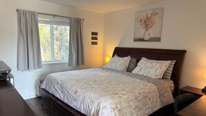 A bedroom with a large bed, a desk, a chair, a window with curtains, and a wall-mounted lamp. - 27 - The family vacation begins! (Challenge-Brownsville)
