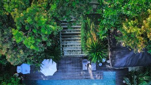 An aerial view of a rooftop pool area with a wooden deck, surrounded by dense greenery and a stone staircase. - Palay (Malay)