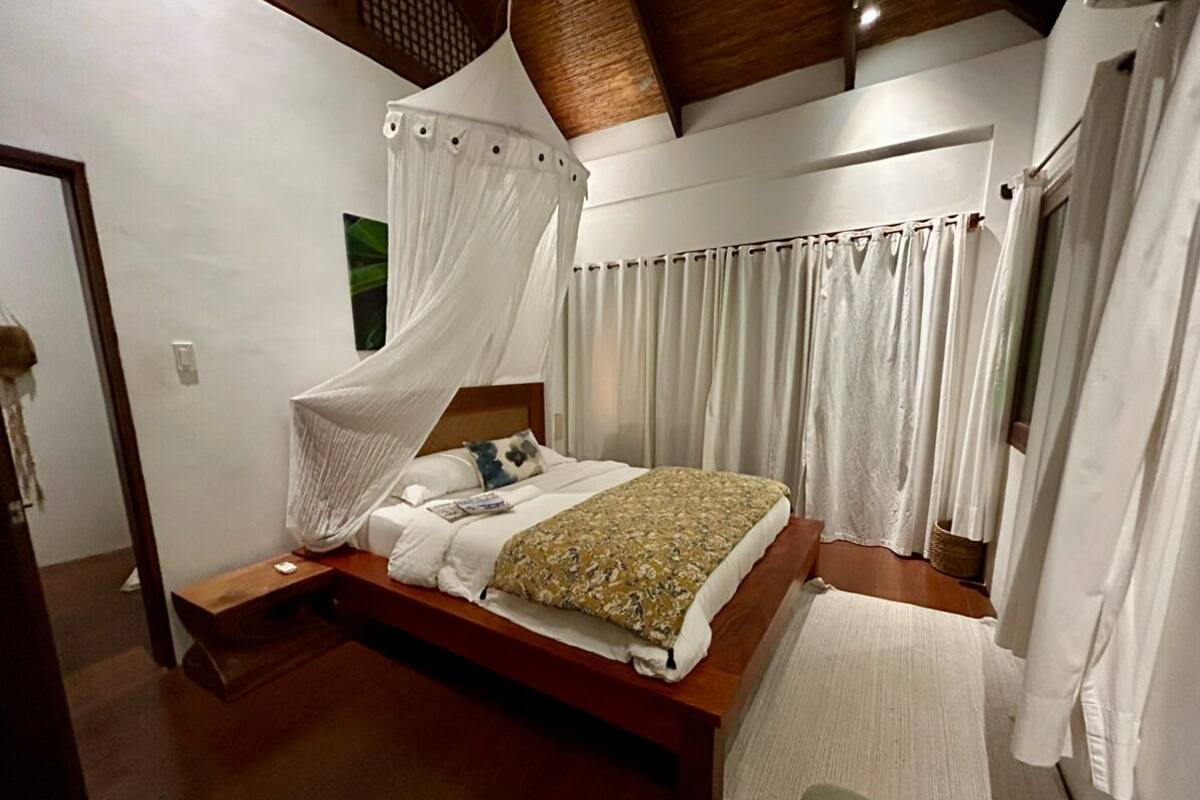 Un dormitorio con cama de madera, cortinas blancas y dosel.