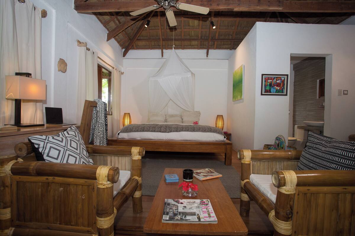 Un dormitorio con cama, muebles de madera, ventilador de techo y mesita de noche con lámpara.