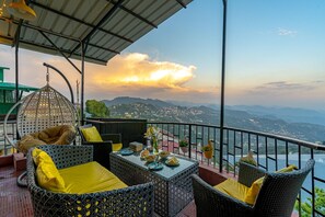A terrace with wicker furniture, a hanging light fixture, and a table set with dishes and a vase. - Artbuzz (Dehradun)