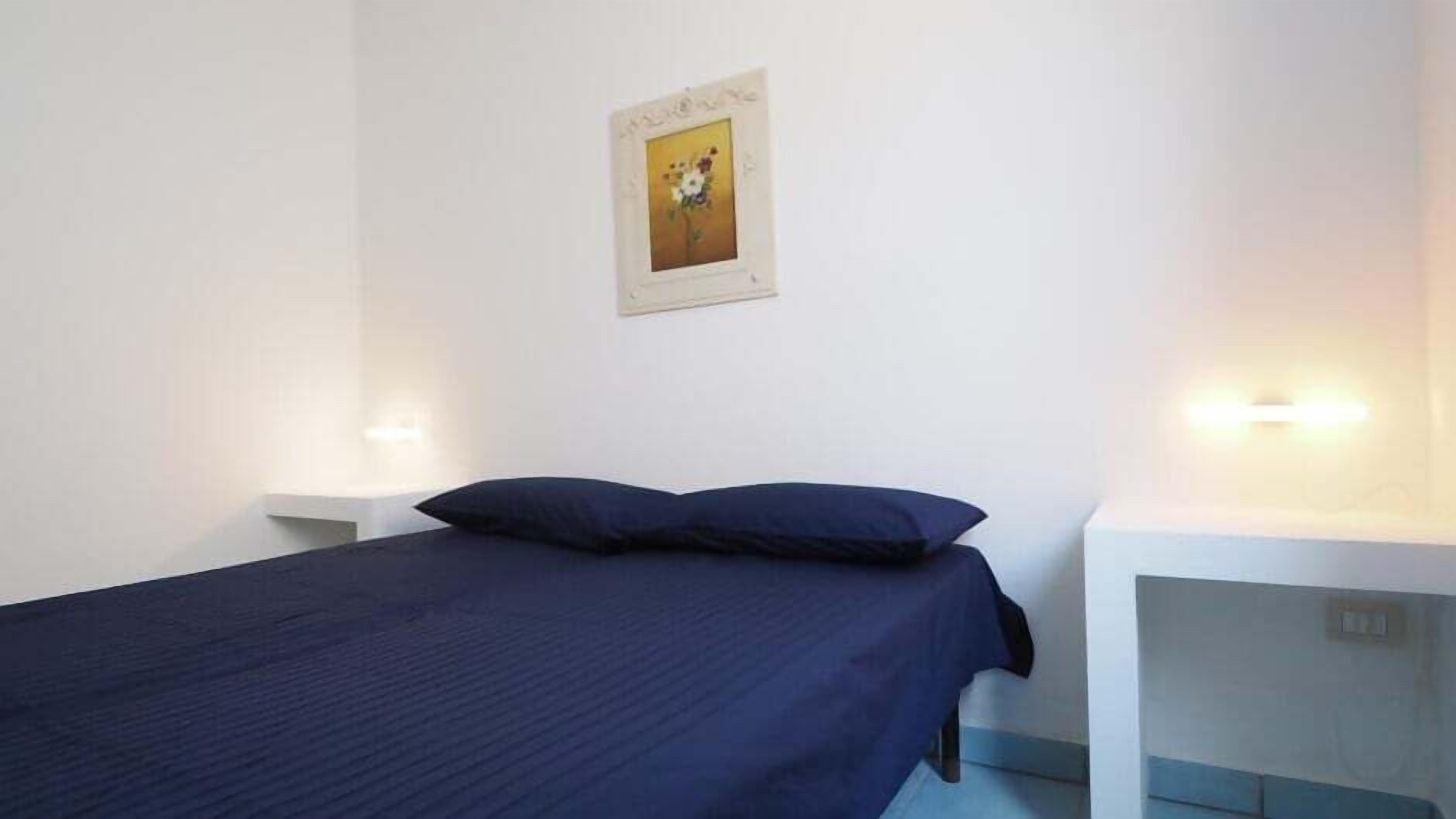 A room with a bed, two bedside tables, and a wall-mounted picture.